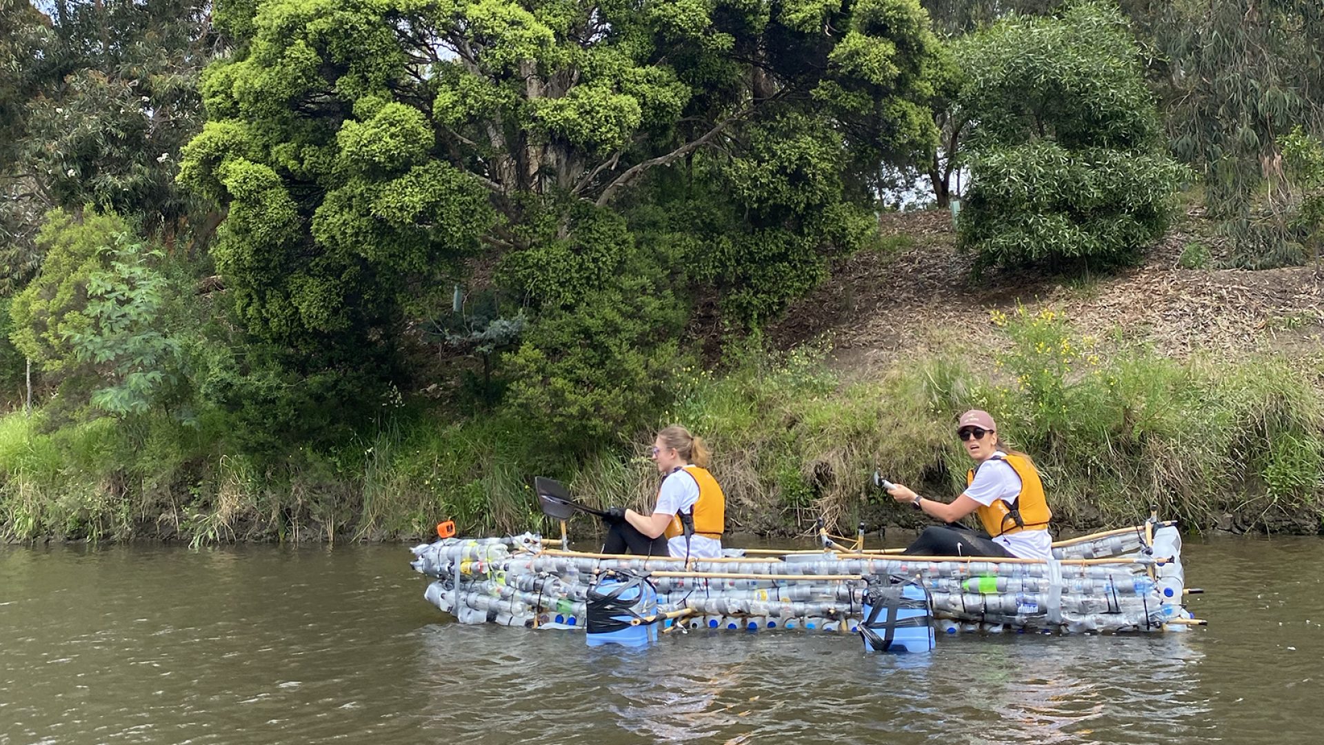 two people in orange life jackets paddle a kayak made out of plastic bottles on a river