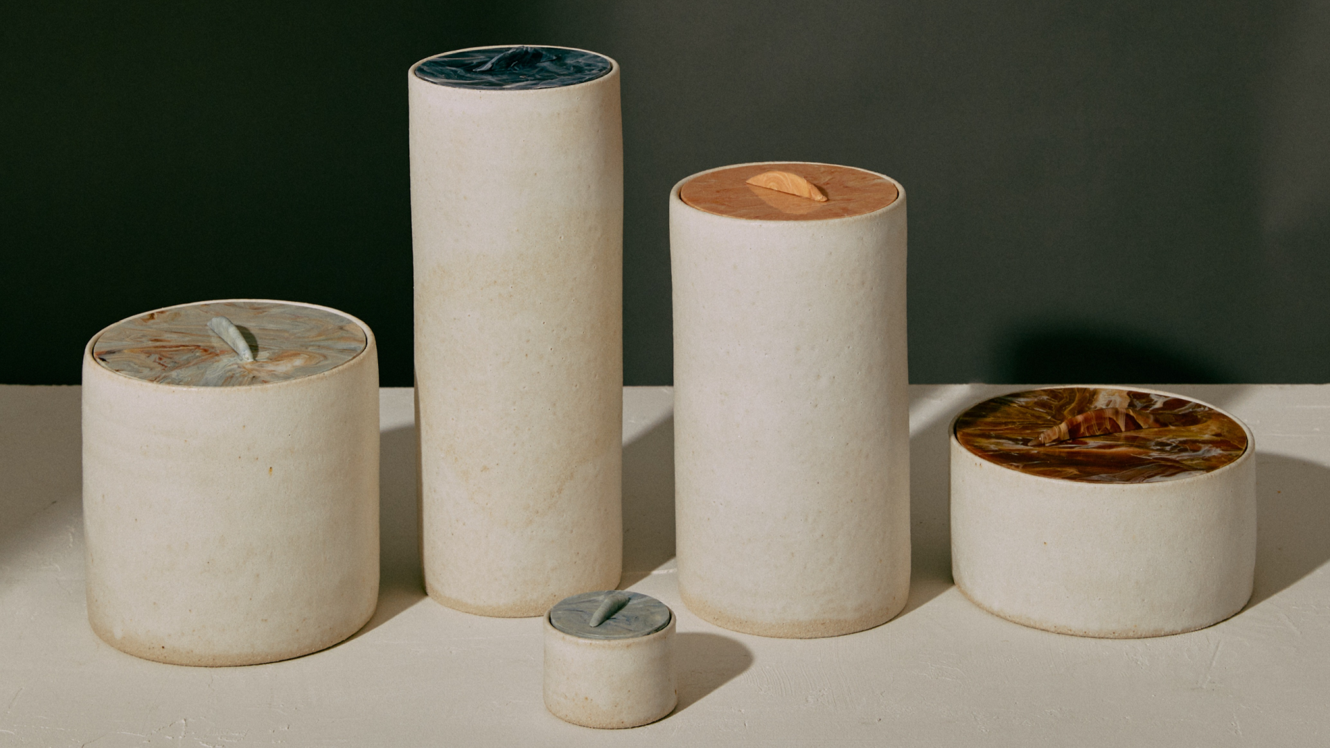Photo of cylindrical white ceramic vessels in varying sizes with colourful marbled plastic lids