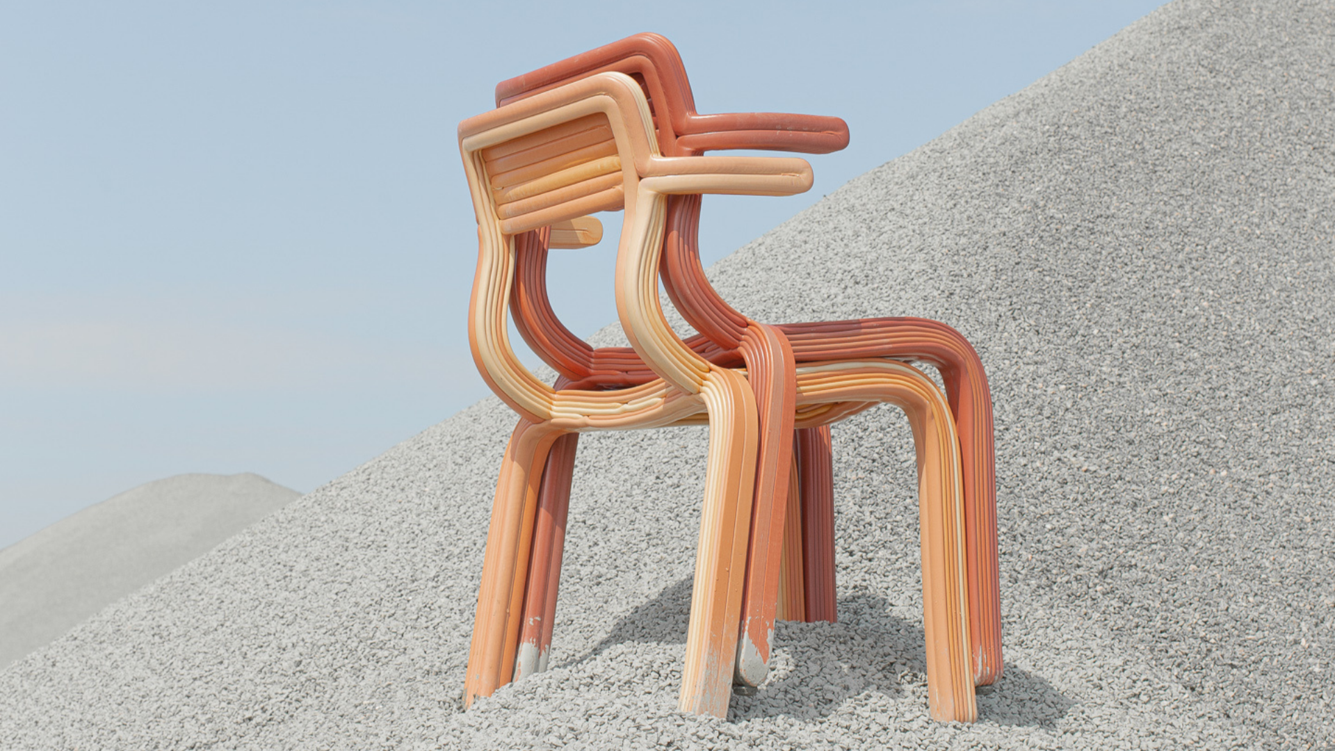 Two stacked chairs made of recycled fridge interiors, shown in an outdoor landscape of rocky terrain. 