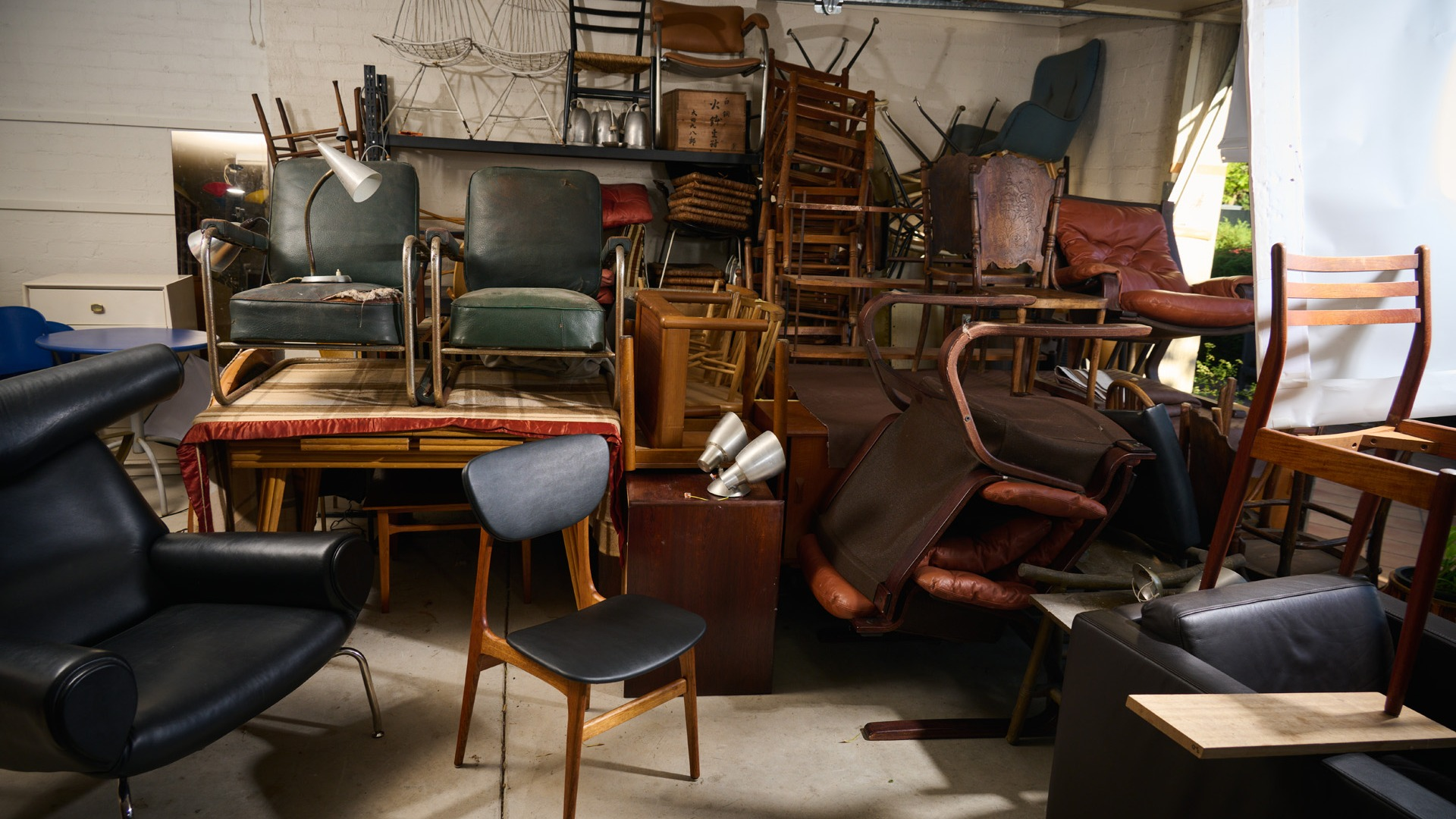 Photo of Edwin Fox Furniture workshop / studio. Collection of furniture and chairs waiting to be restored. 